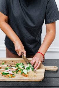 Close-up of a person slicing fresh vegetables on a wooden cutting board, top view.